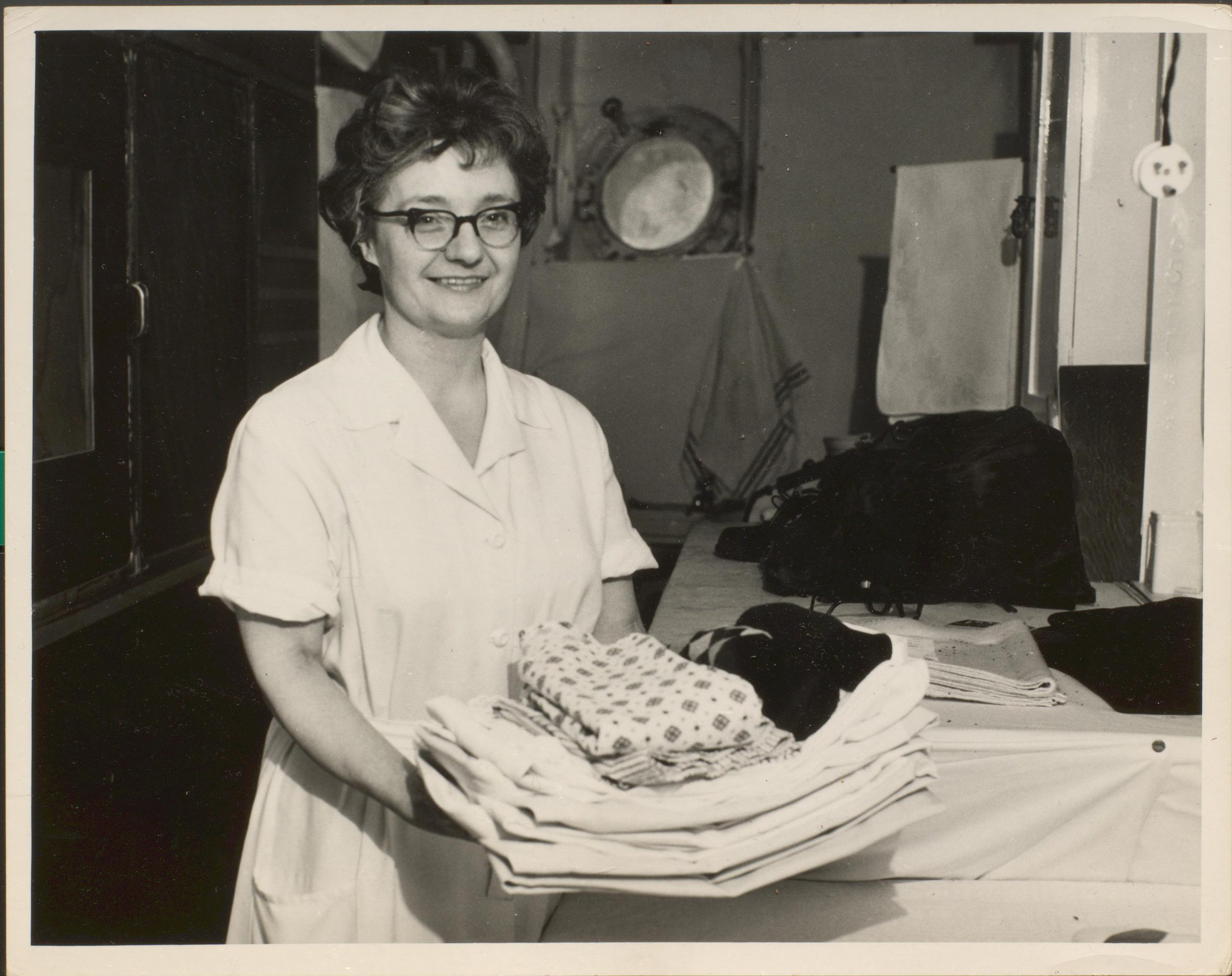 Black and white photograph of female in uniform carrying a pile of folded laundry.
