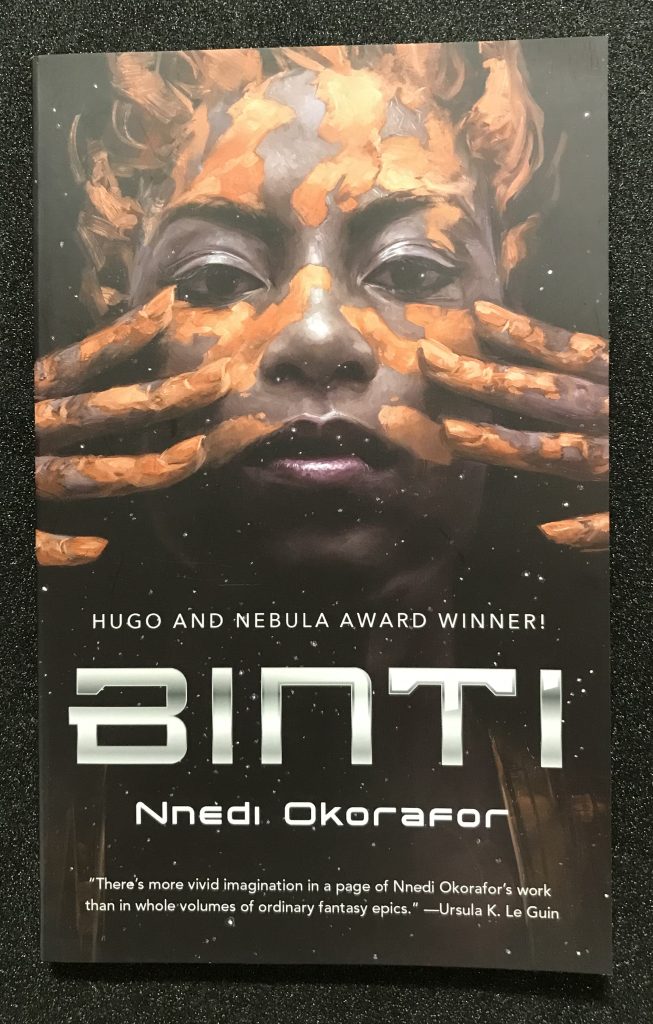 Book cover showing face with smeared red clay and two hands placed on either cheek.